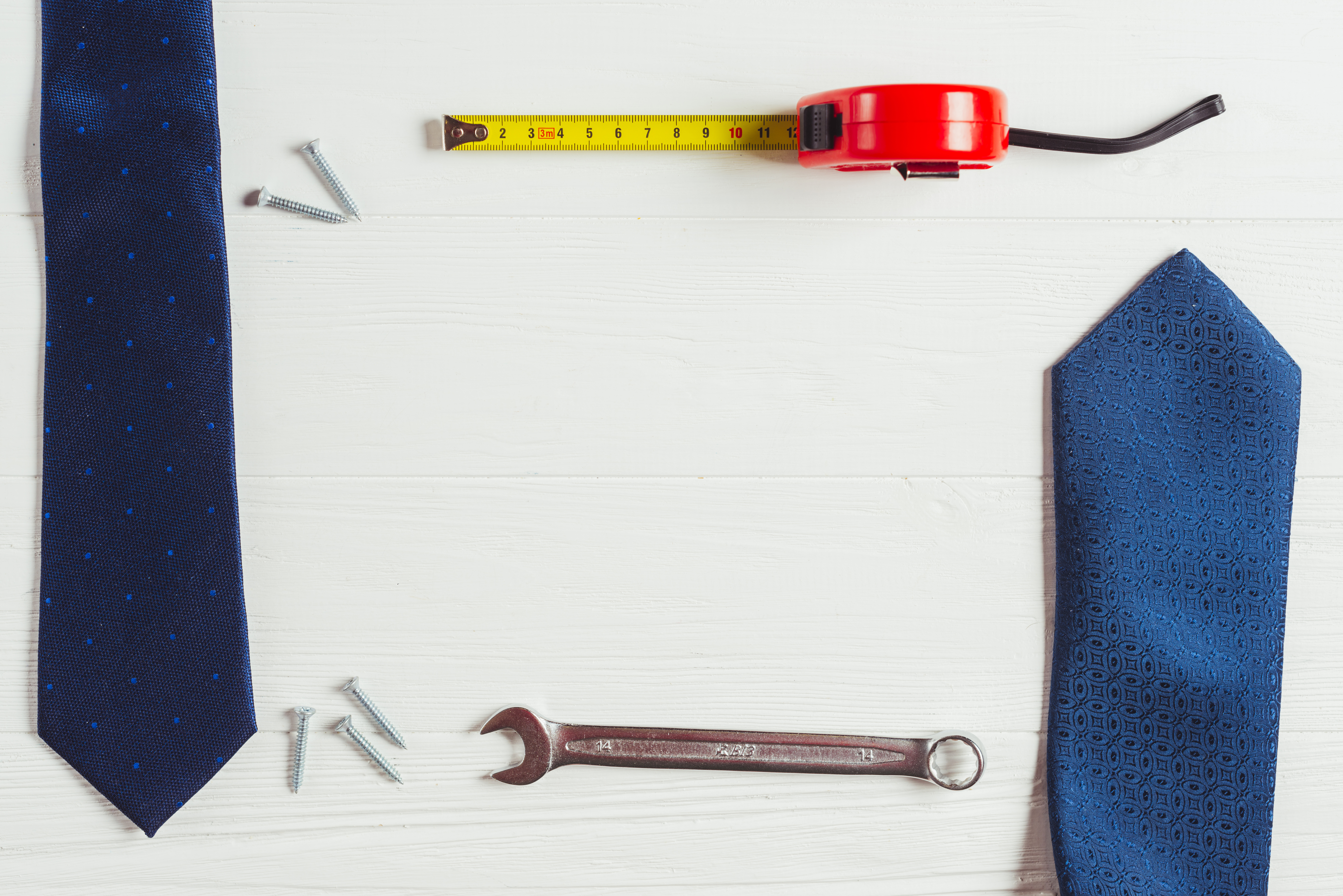 Blue neckties arranged beside a wrench, screws, and a measuring tape on a white surface, symbolizing the convergence of white-collar and skilled trades careers in the AI-driven workforce.